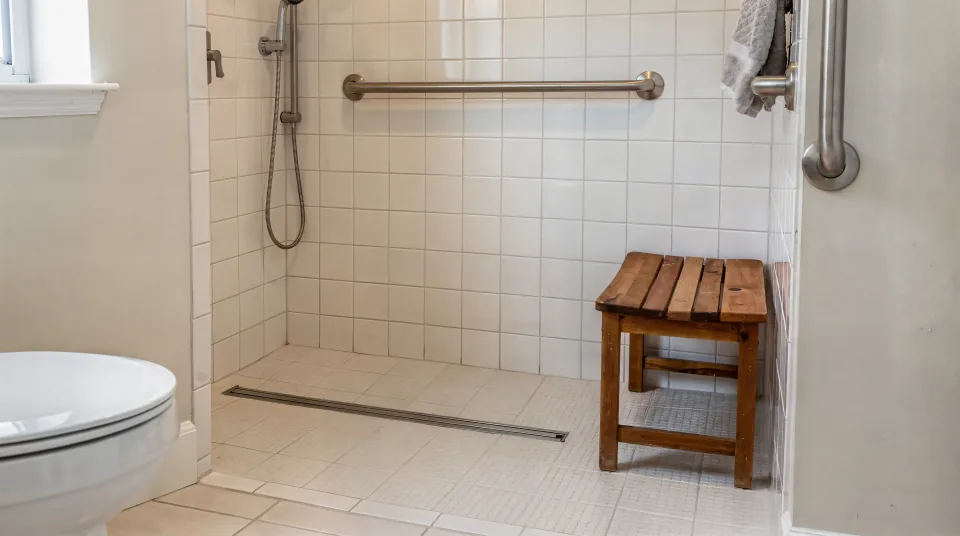 Zero-threshold walk-in shower with a freestanding wooden shower seat, two grab bars, a hand-held shower and a comfort-height toilet