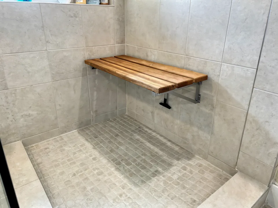 Textured slip-resistant porcelain floor tile being set with a freestanding wooden shower seat bracket on the wall
