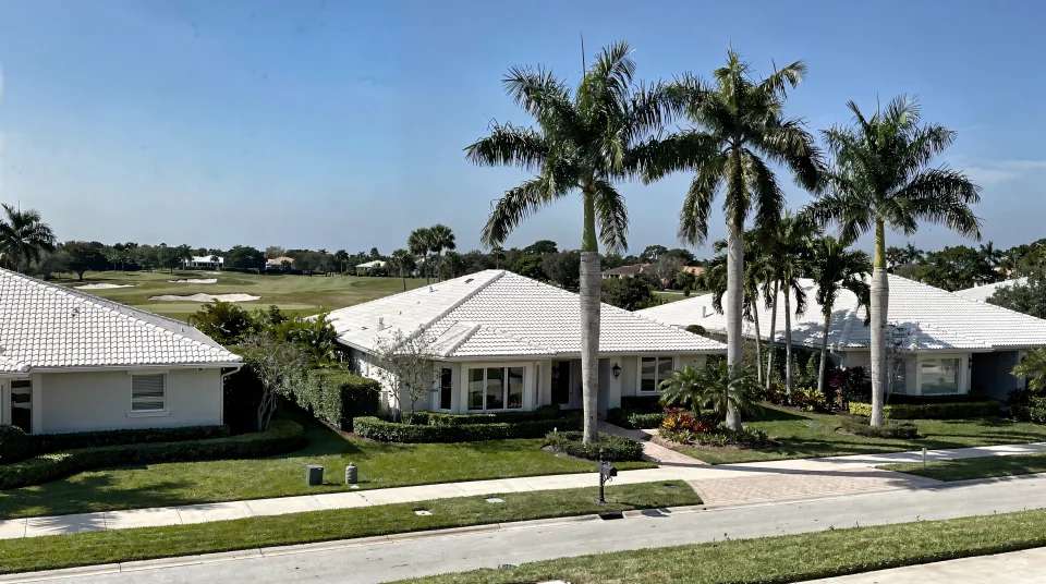 Boca Raton country-club street with large one-story homes, white barrel-tile roofs, clipped hedges and a golf fairway behind