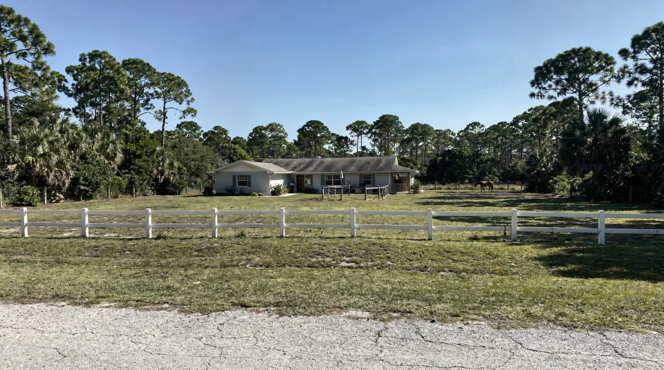Davie ranch house set back behind a white rail fence with a pasture and slash pines