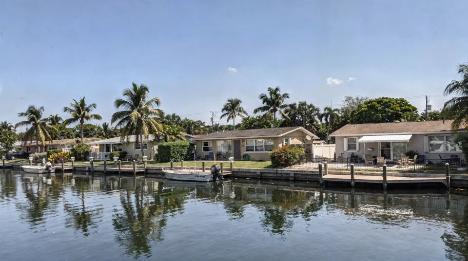 Canal-front Fort Lauderdale neighborhood with mid-century single-story homes, a small boat at a dock and coconut palms