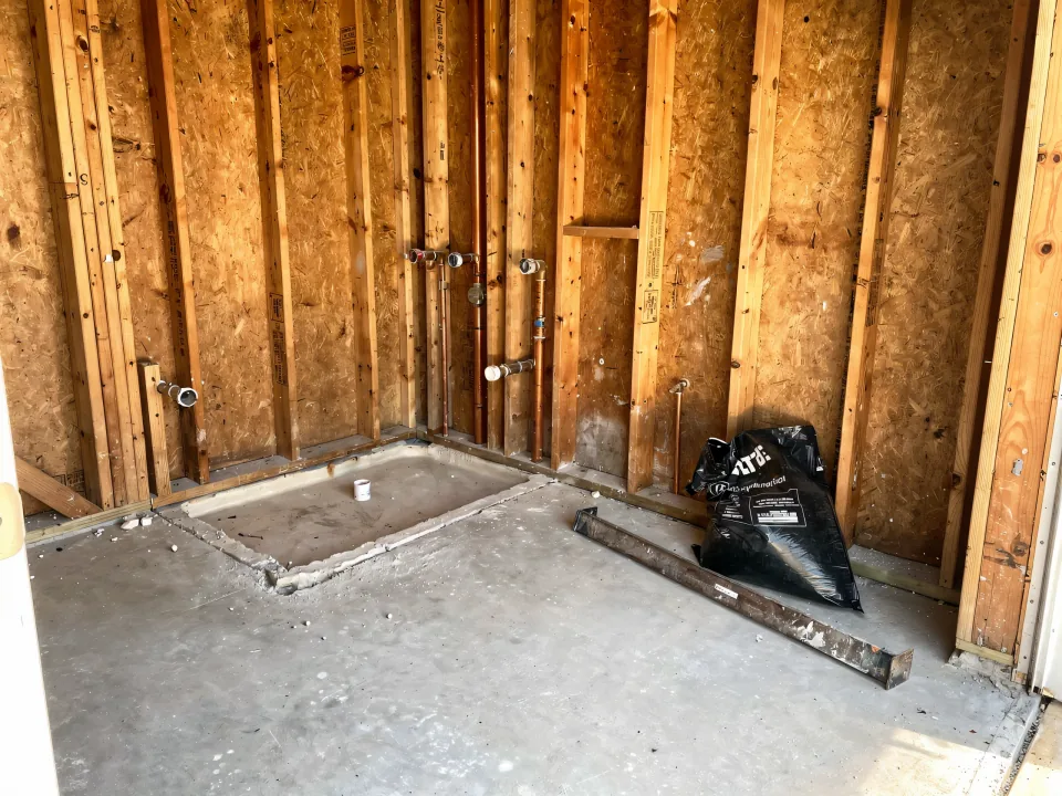 Bathroom demolished to bare wood studs with the old tub removed and the slab floor swept clean
