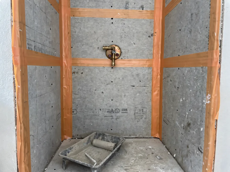 Cement board shower walls with orange waterproofing membrane at the seams and a new valve rough-in