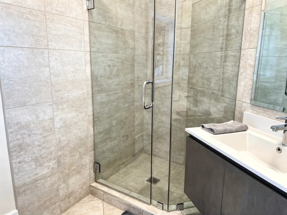 Finished bathroom with grouted tile walls, a floating vanity, a glass shower door and a folded towel