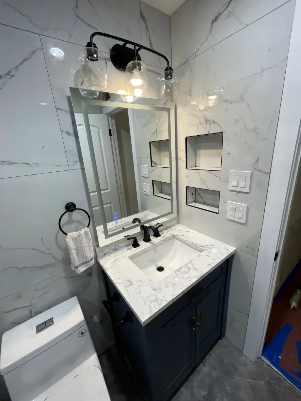 The same bathroom after the remodel with custom tile, black hardware and a lit mirror