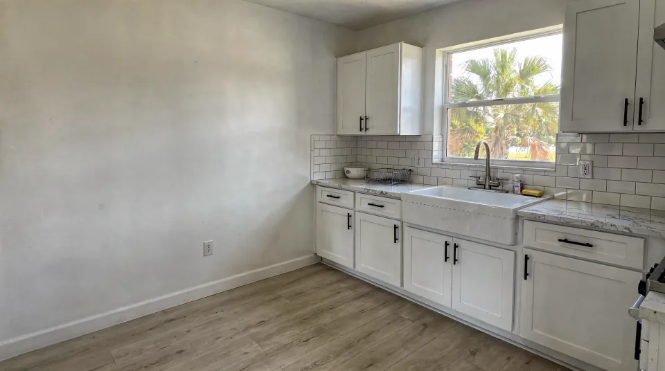 Remodeled kitchen with white shaker cabinets, a quartz counter, a subway tile backsplash and a farmhouse sink under a window