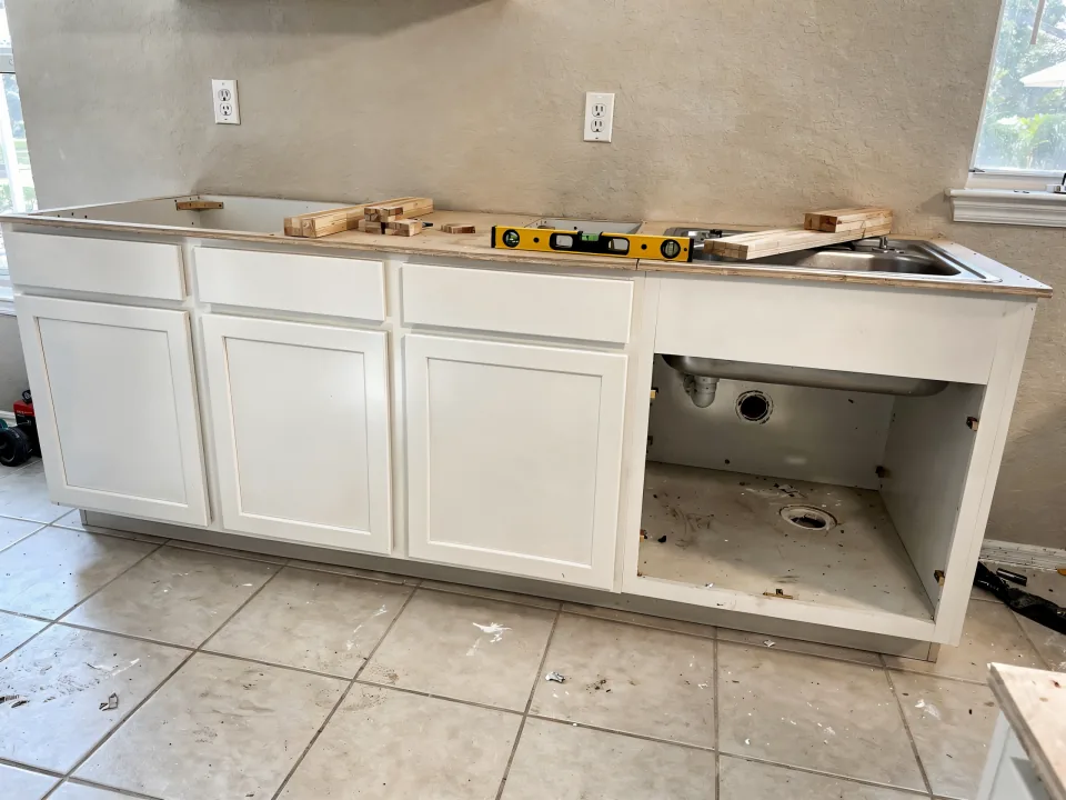 New white shaker base cabinets installed and leveled along a kitchen wall with shims and a level on top