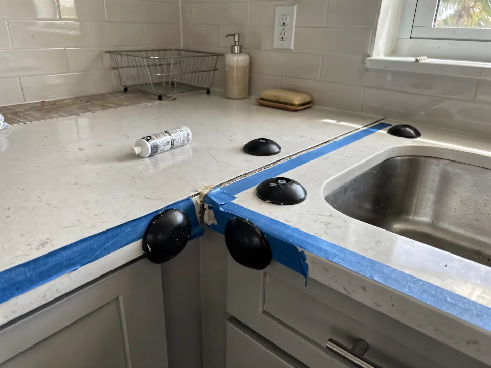Quartz countertop slab being set on new cabinets with suction cups and tape on the edges