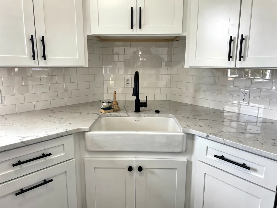 Finished kitchen corner with white shaker cabinets, a quartz counter, subway tile and a farmhouse sink