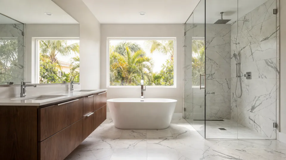 Primary bathroom with a 72-inch walnut double vanity, a freestanding tub under a window and a curbless marble-look shower behind frameless glass