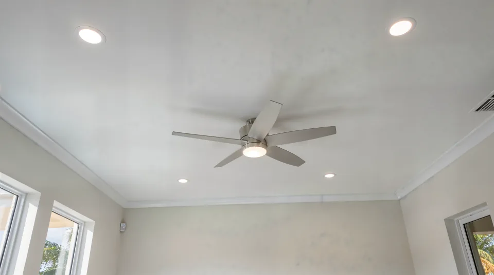Finished family room ceiling in smooth flat white with crisp corners where the walls meet, recessed lights and a ceiling fan, popcorn texture gone