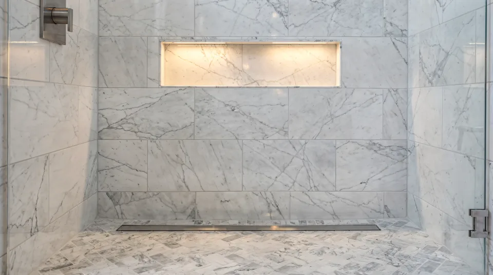 Tiled shower with 24 by 48 marble-look porcelain walls, a herringbone mosaic floor sloping to a linear drain and a recessed niche lit from above