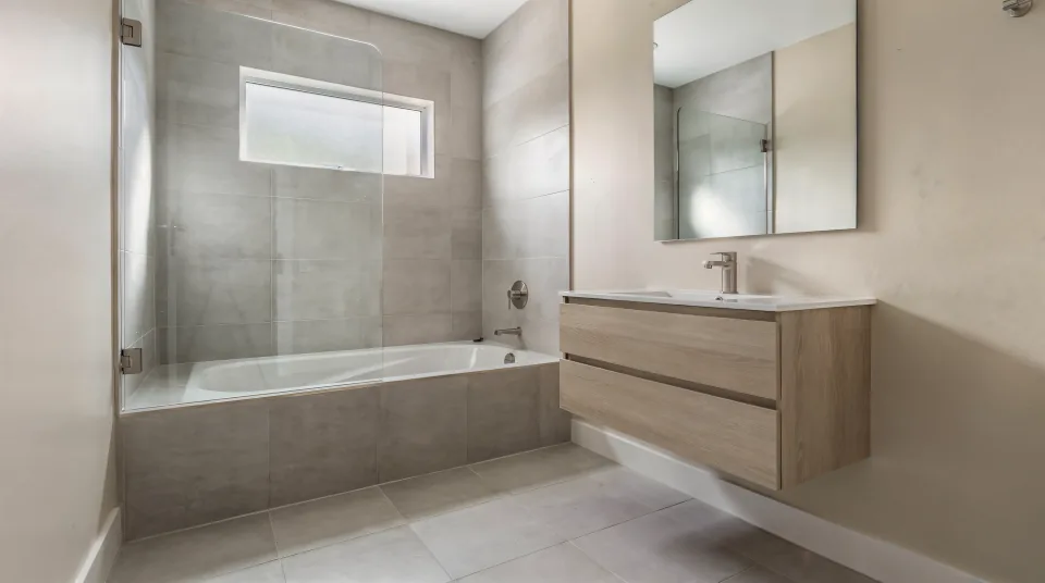Small 5 by 8 hall bathroom finished with a wall-hung white oak vanity, large-format pale grey tile and a fixed glass panel on the tub