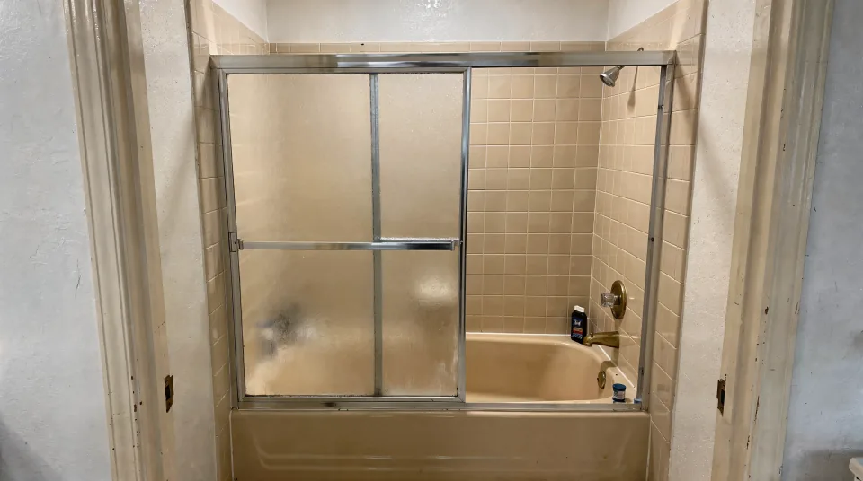 Dated 1980s tub alcove with almond tub, beige tile surround and a sliding frosted glass door