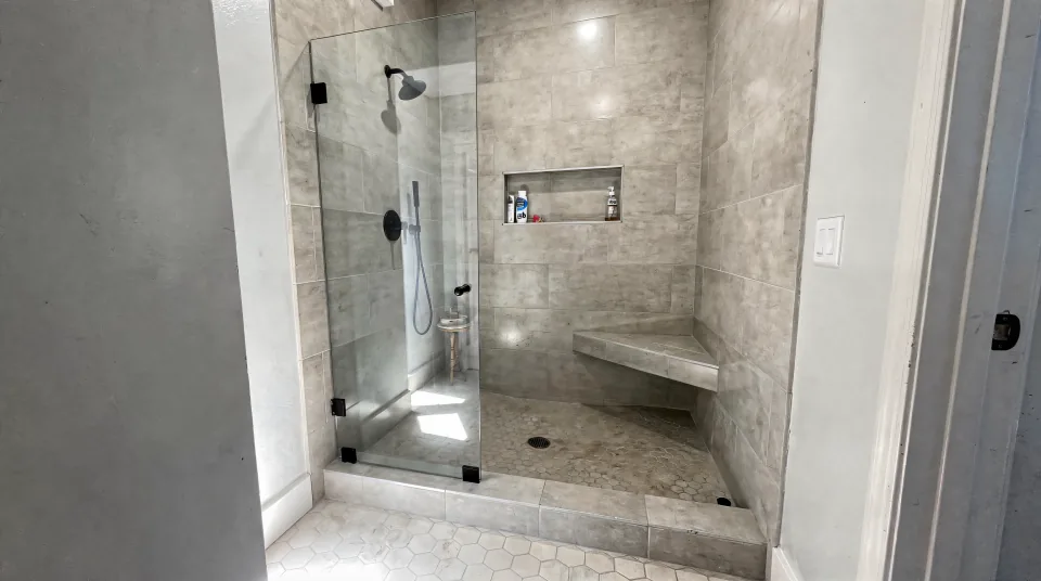 Tub alcove converted to a walk-in shower with a low tiled threshold, greige porcelain walls, a bench and a frameless glass panel