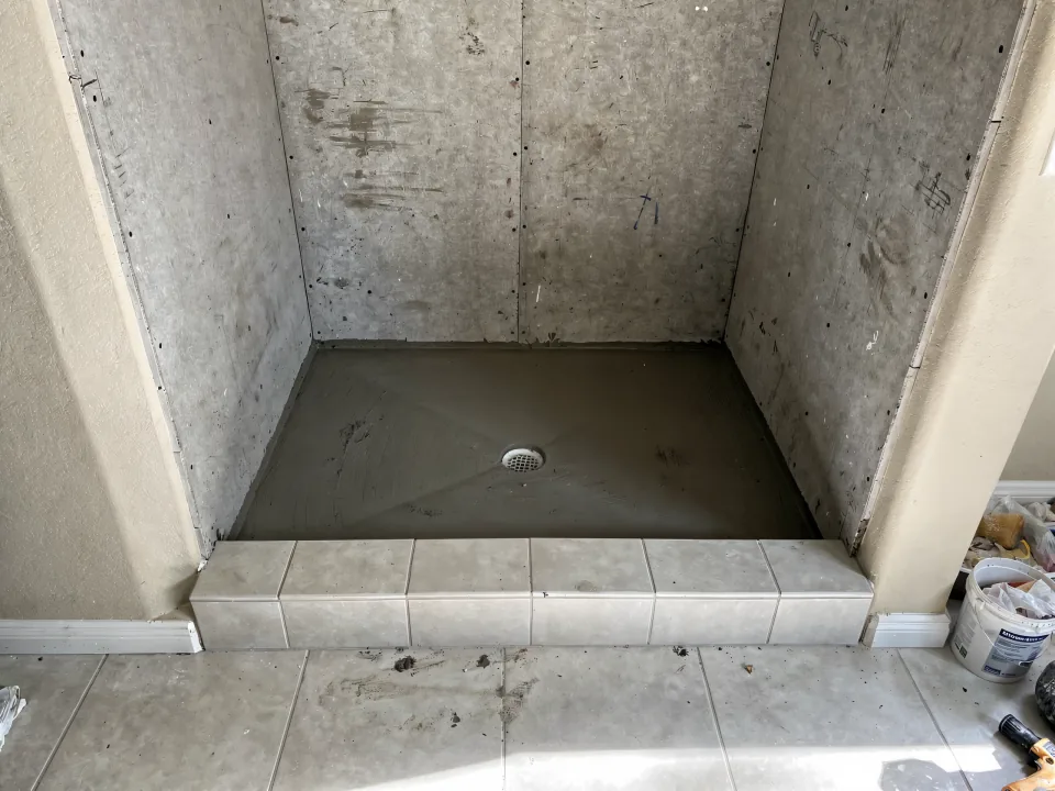 New mortar shower pan sloped to a center drain with a framed low curb and cement board walls