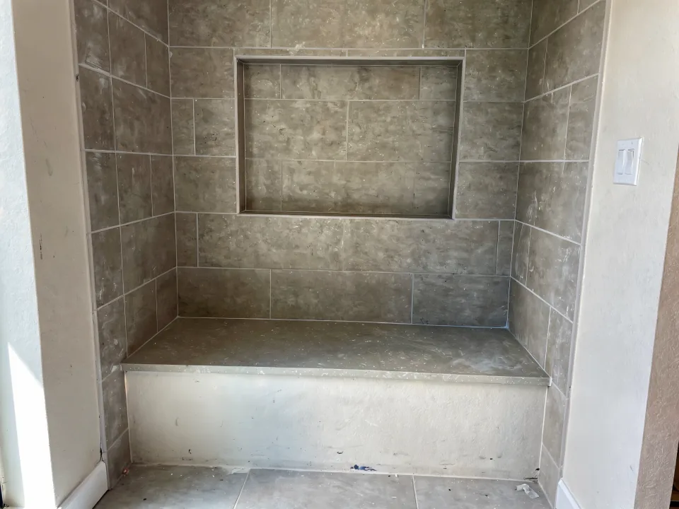 Tile set to shoulder height in a converted alcove with a tiled niche and a bench waiting for its top