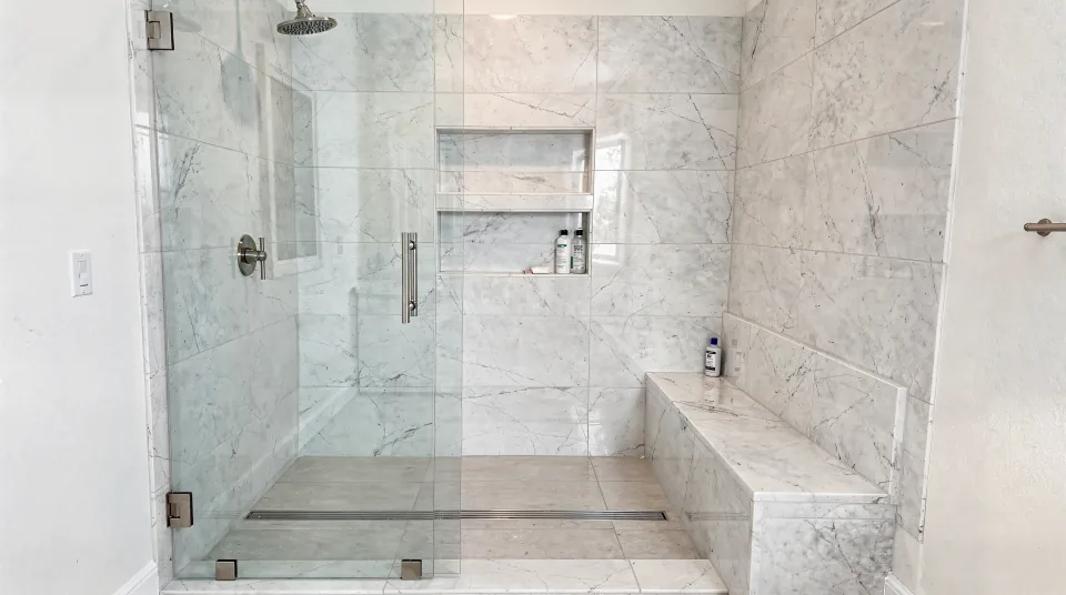Curbless walk-in shower with a linear drain, marble-look porcelain, a built-in bench and a frameless glass panel