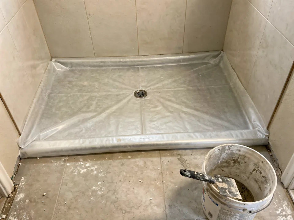 Curbless shower with a sloped mortar bed and a sheet waterproofing membrane folded up the walls
