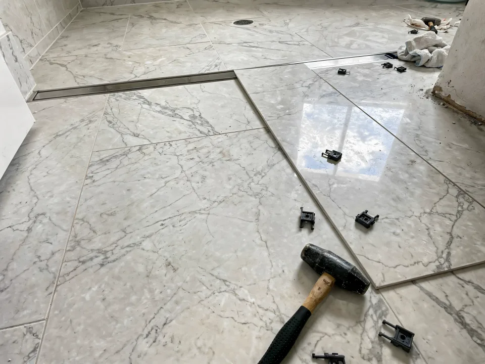 Marble-look porcelain being set on a curbless shower floor sloping to a linear drain