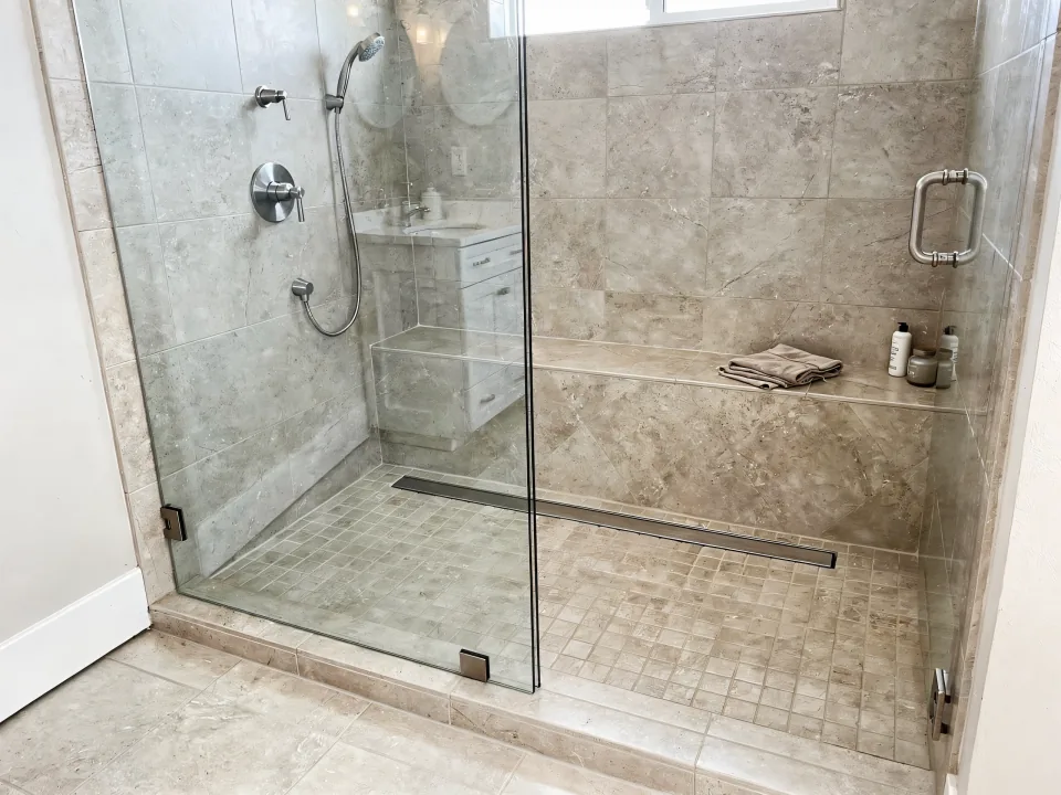 Finished curbless walk-in shower with continuous floor tile, a linear drain, a frameless panel and a built-in bench